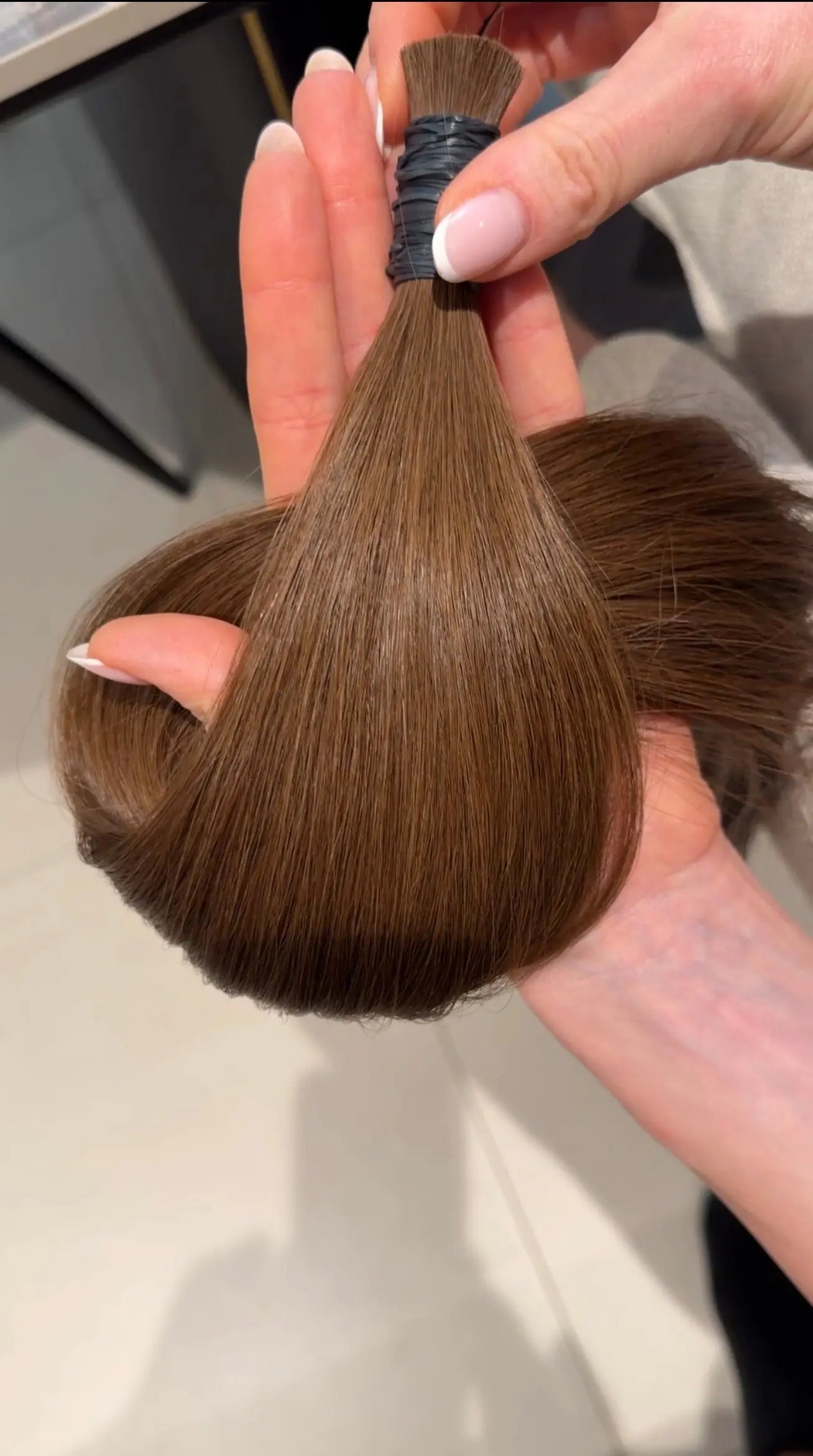 Number 6 hair extensions held by a person's hand against a neutral background