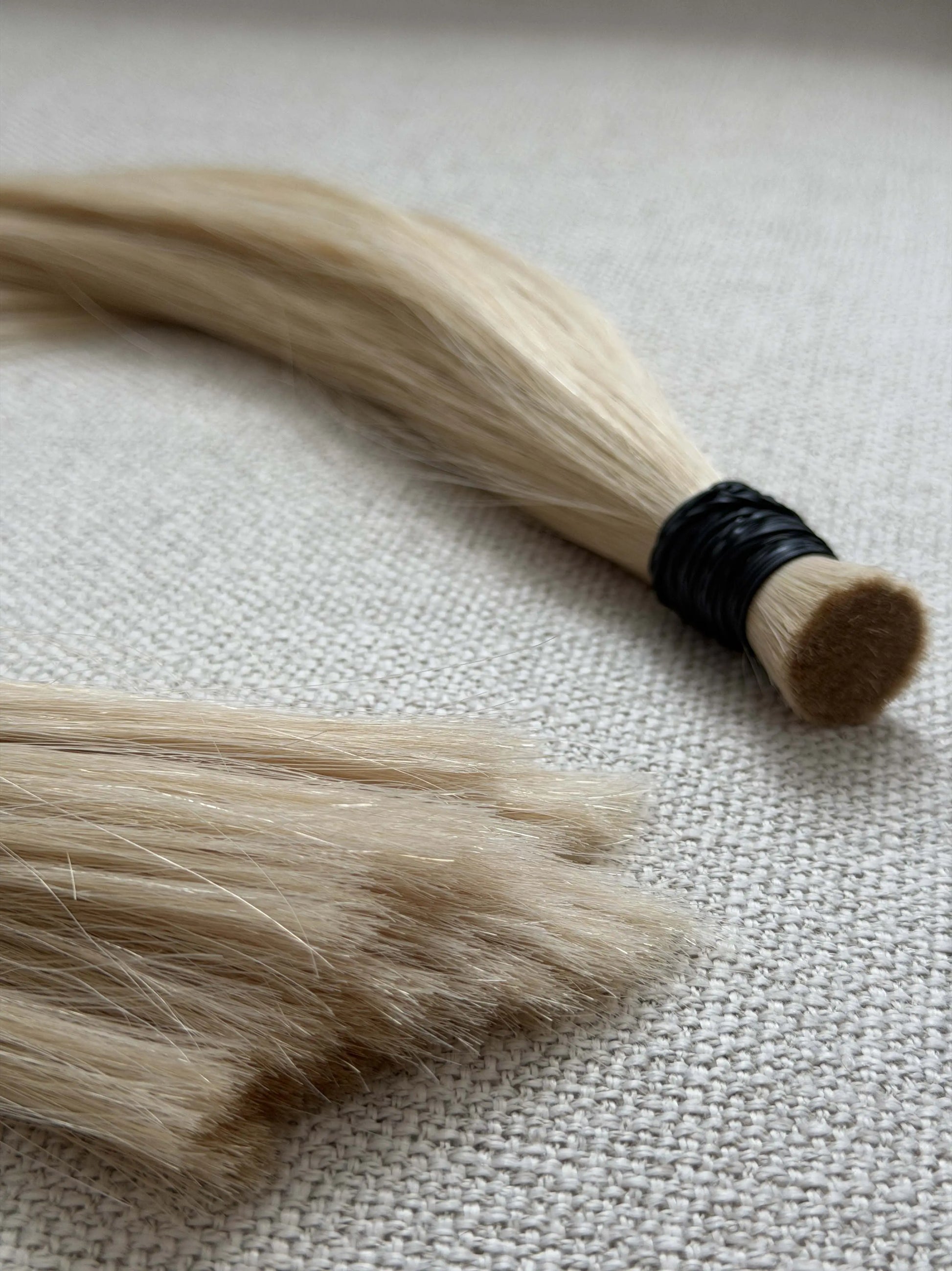 Blonde number 60 hair extensions with a black band on a textured beige surface