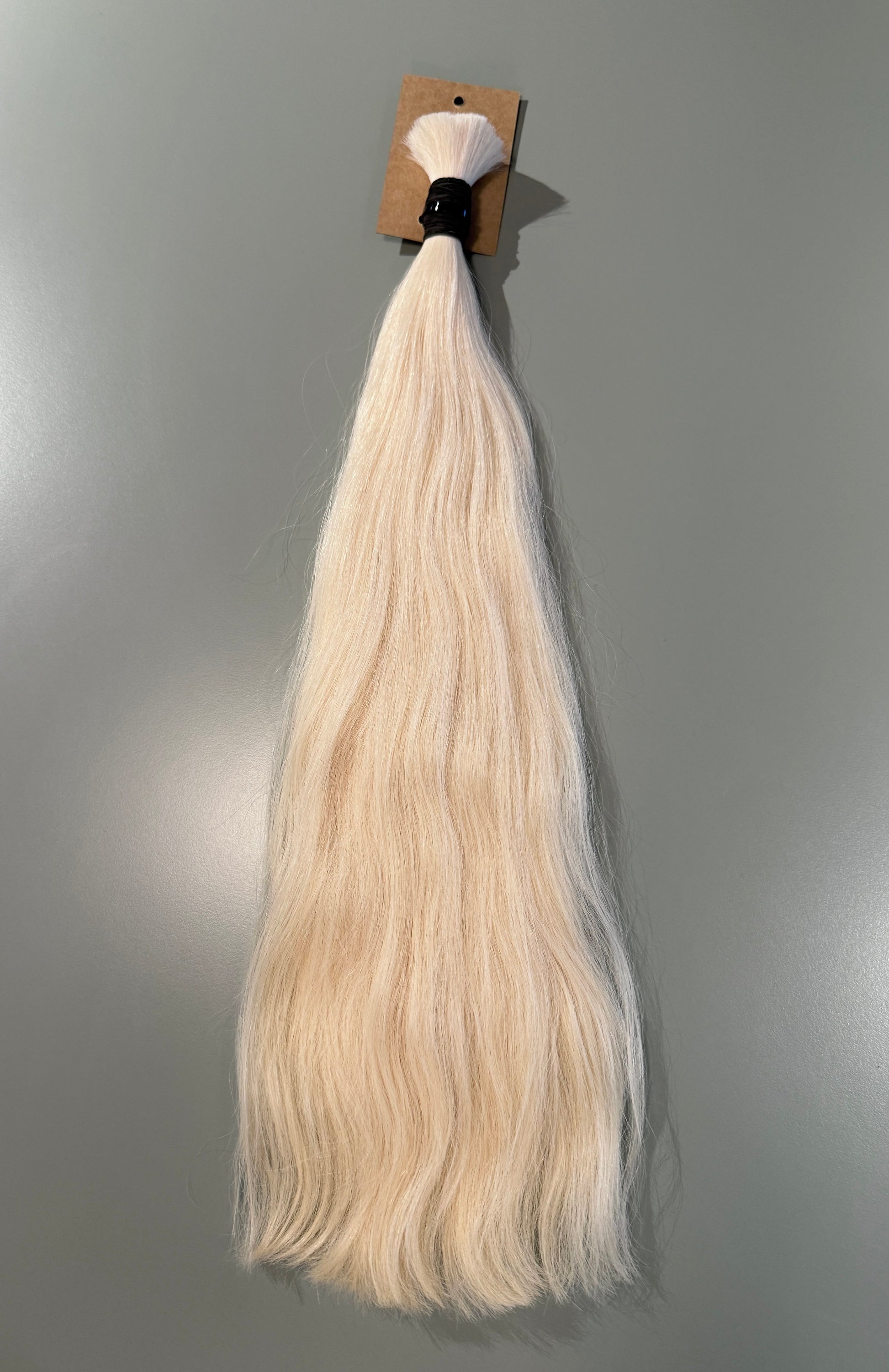 A bundle of long, straight blonde slavic hair extensions with a black band and brown cardboard header, shown against a plain gray background.