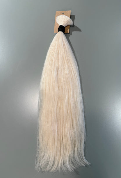 A bundle of long, straight Slavic hair extensions in a light platinum blonde color, attached to a small cardboard display card with a black elastic band, shown against a plain gray wall.