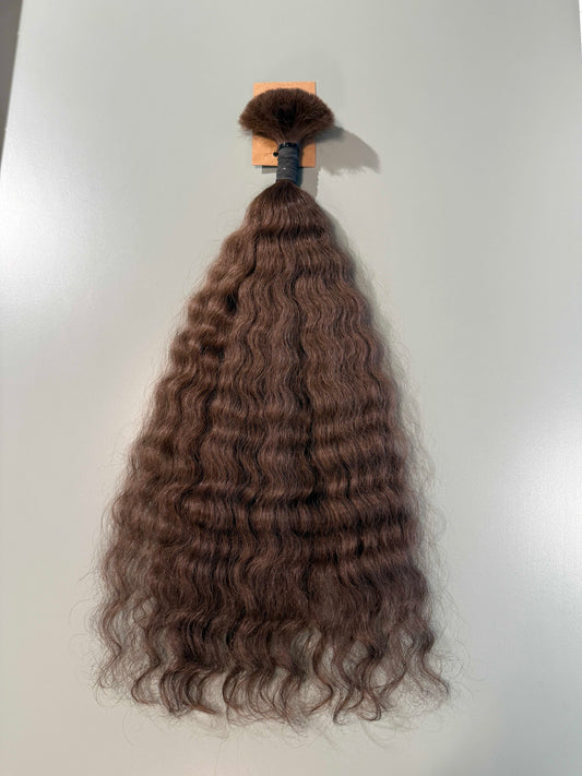 A bundle of long, dark brown wavy Slavic hair extensions with a black clip and a small orange paper tag, displayed against a plain light gray background.